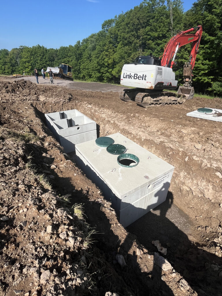 Excavator installing precast concrete septic tanks at construction site