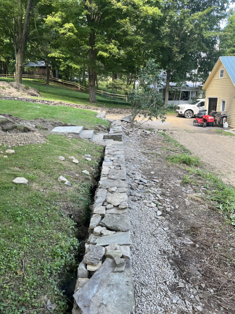 Stone drainage ditch installation beside residential driveway and yard